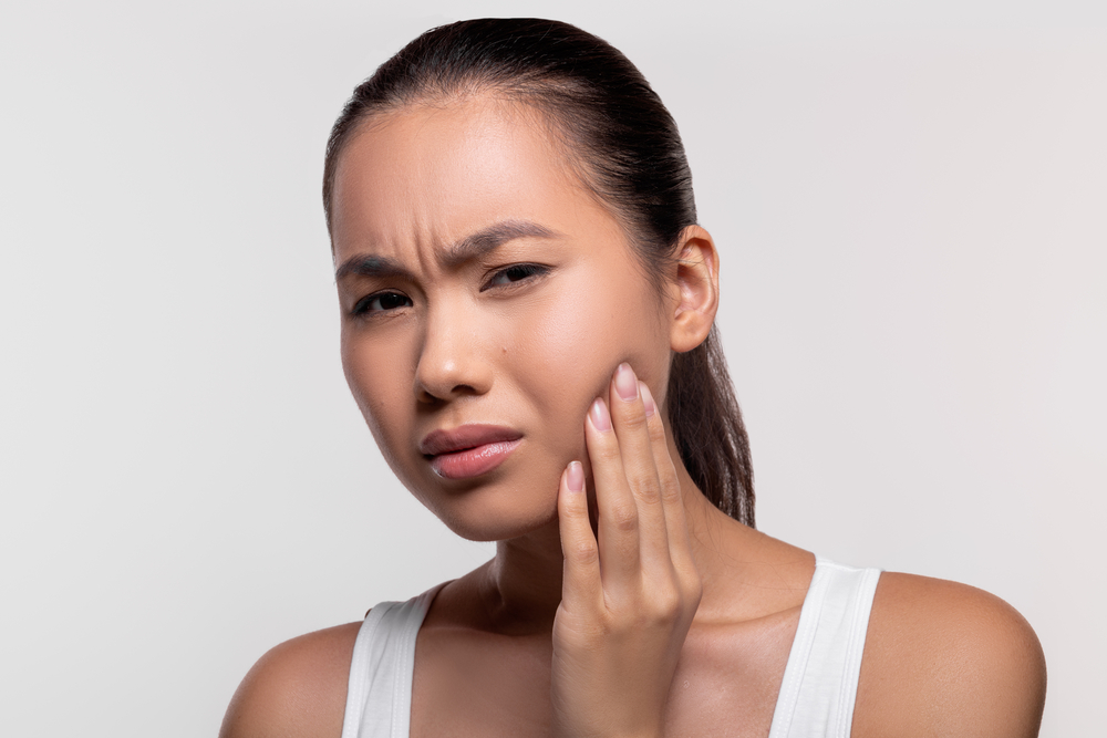 Young woman with wisdom tooth pain holding her hand to her cheek.