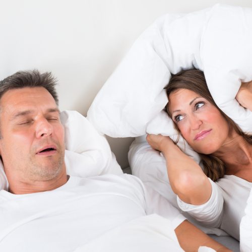 Woman covering her ears with pillow while man is snoring